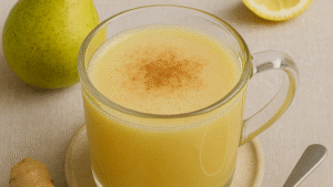 Picture of a glass coffee mug filled to the top with Ginger Pear Elixir. A pear and a lemon sitting on the table in the background.